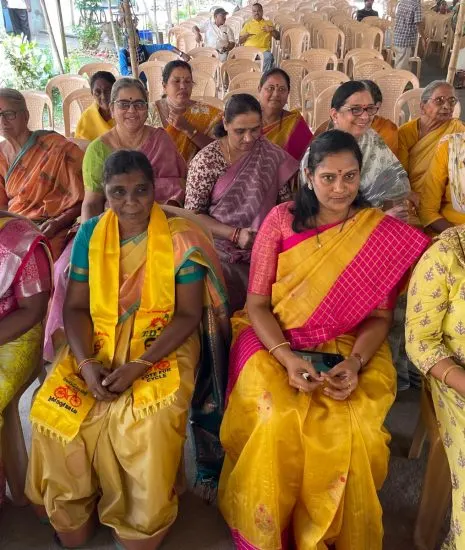 Women of the Mahila Jagruthi wing seated in rows at an open-air constituency meeting, one wearing a TDP "Vote for Cycle" scarf.